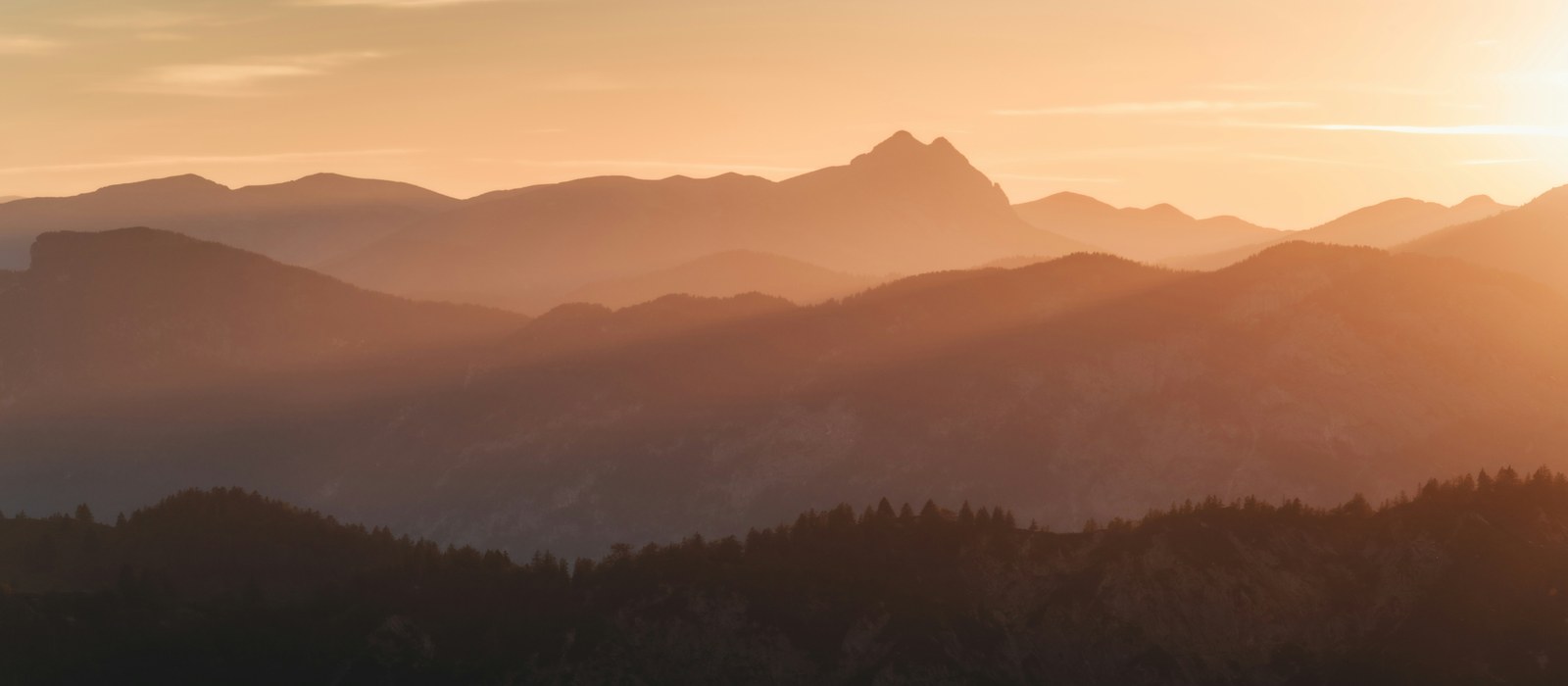 Golden sunset over layered Alpine mountain silhouettes in Austria